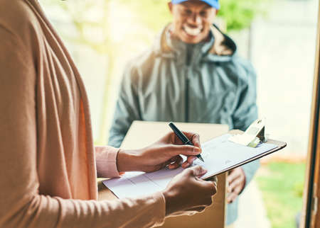 All thats needed is a simple signature. Shot of a woman signing for her delivery from the courier.の写真素材