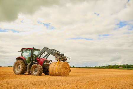 His farm is well-kept. Shot of a farmer stacking hale bales with a tractor on his farm.の写真素材