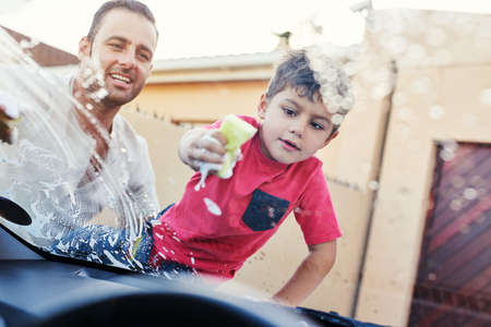 This car is going to be squeaky clean. Shot of a family washing their car in the driveway.の写真素材