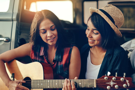 Music makes the memories. Shot of a young woman playing a guitar on a road trip with her friend.
