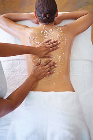 On her way to smooth, silky skin. Rearview shot of a woman getting an exfoliation treatment.の写真素材