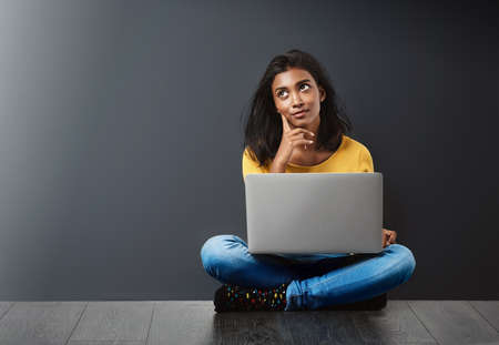 Should I post that. Studio shot of an attractive young woman using a laptop against a gray background.の写真素材