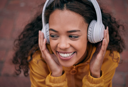 I could listen to this on repeat. Cropped shot of a beautiful young woman wearing headphones while standing outside.の写真素材