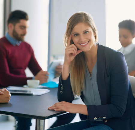 Success starts now. Portrait of a young entrepreneur sitting in an office with her colleagues in the...