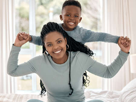 Mommys favourite boy. Cropped portrait of an attractive young woman sitting on the bed at home with her son on her back.の写真素材