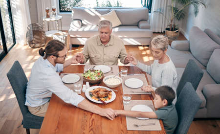 Bless the food before us and the family beside us. Shot of a family holding hands in prayer before having a meal together at home.の写真素材