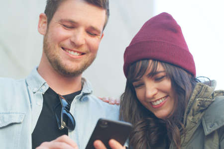 Good news will always leave a smile on your face. Cropped shot of an affectionate young couple using a cellphone together outdoors.の写真素材