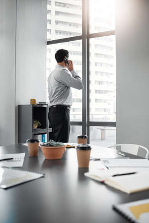 Making big decisions. Shot of an unrecognisable businessman standing alone in the office and using his cellphone.の写真素材