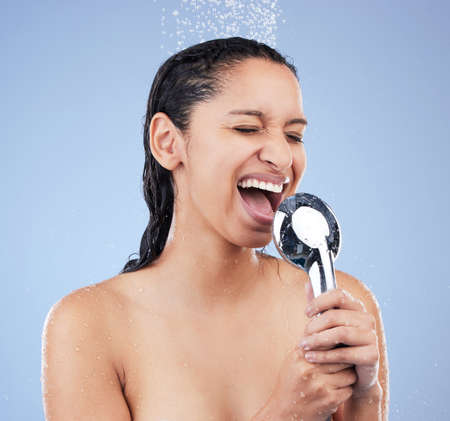 Time for my one man concert. Shot of a young woman taking a shower against a blue background.の写真素材