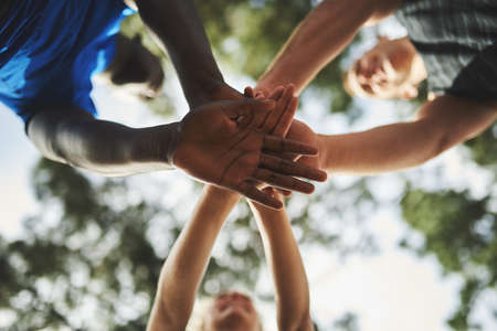 Its easier when you have support. Low angle shot of a group of sporty young people holding their hands together in unity.の写真素材