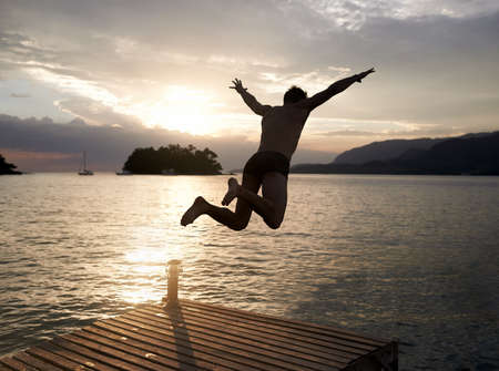 Spontaneity at sunset. Rear view shot of a young man diving off the jetty into a lake at sunset.の写真素材