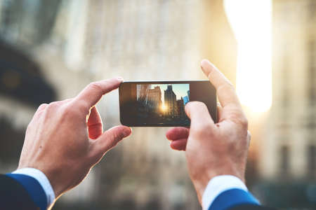 Well hello there morning sun. Shot of an unrecognizable man taking a picture of the sun rising over buildings in the city during the morning hours.の写真素材