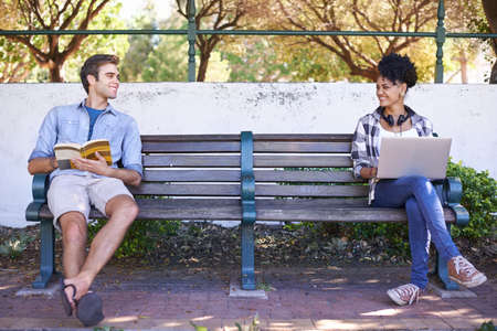 Noticing each other for the first time. Two students sitting on opposite sides of a bench with their reading material in front of them and looking at each other.の写真素材