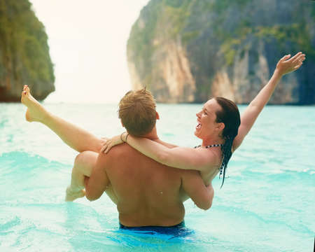 Theres no one Id rather vacay with. Rearview shot of a man carrying his happy girlfriend into the sea.の写真素材