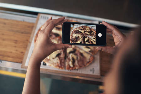I have to put this on my blog. Cropped shot of an unrecognizable woman sitting alone and using her cellphone to photograph her pizza at a restaurant.の写真素材