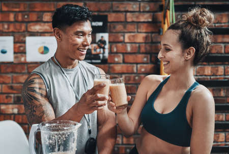 Cheers to a fit and healthy life. Cropped shot of two young sportspeople making a toast with milkshakes while working in a gym.の写真素材