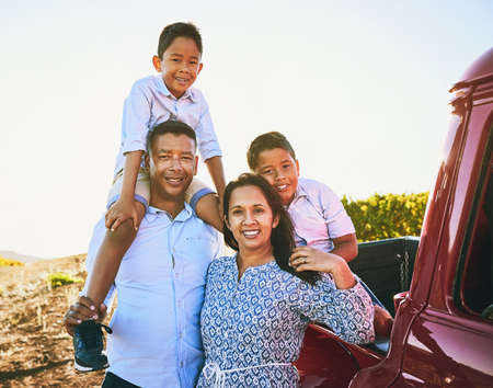 On a road trip with the family. Shot of a cheerful family posing for a portrait together outside next to a red pickup truck.の写真素材