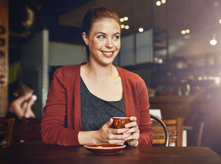 This is by far my favorite cafe. Cropped shot of a young woman having a cup of coffee in a cafe.の写真素材