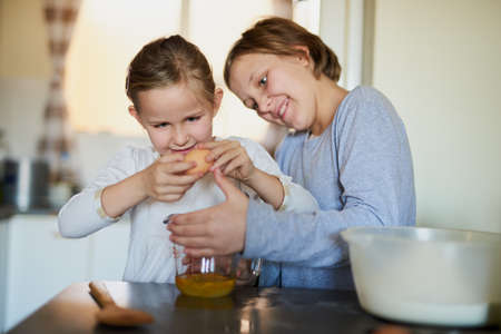 Try not to get any shells in. Cropped shot of two young siblings baking together at home.の写真素材