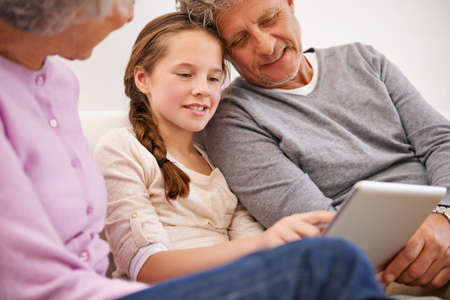 And thats the world of social media. Shot of grandparents watching their granddaughter use a digital tablet.の写真素材
