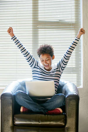 This is just the start of many more great things. Shot of a young woman looking at her laptop with her arms raised in celebration.の写真素材