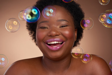 Bubbling beauty. Studio portrait of a beautiful young woman looking happy against a brown background surrounded by bubbles.の写真素材
