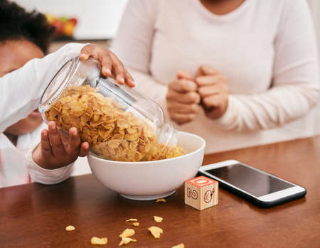 She cant get enough of it. Shot of a girl messing as she pours cereal into a bowl.の写真素材