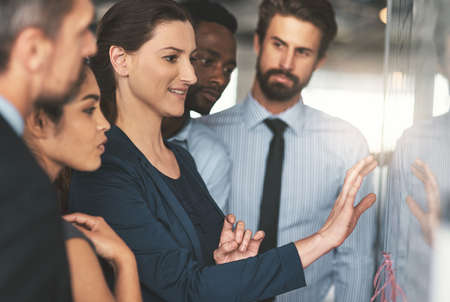 Everyone is in on the plan. Shot of a group of businesspeople looking over plans on a whiteboard.の写真素材
