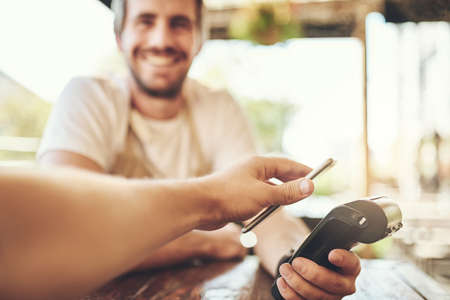 Pay the smart way. Cropped shot of a customer making a wireless payment in a coffee shop.の写真素材