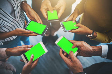 Get your word out there to the world. Closeup shot of an unrecognizable group of businesspeople using their cellphones in synchronicity.の写真素材
