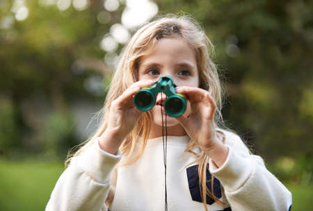 Shes a budding Ornithologist. An adorable young child holding binoculars outdoors.