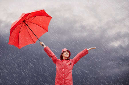 The rain makes me happy. A beautiful young woman standing outside with her red umbrella.の写真素材