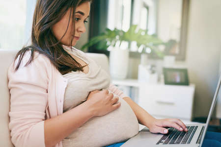 Blogging with a baby on board. Cropped shot of an attractive young pregnant woman working from home.の写真素材