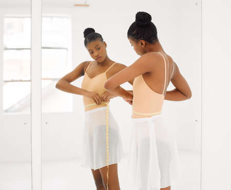 Dont let insecure thoughts ruin something amazing. Shot of a beautiful young ballet dancer measuring her waist during a rehearsal.の写真素材
