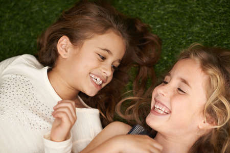 Pure childhood delight. Cropped shot of two little girls lying on their backs outside.