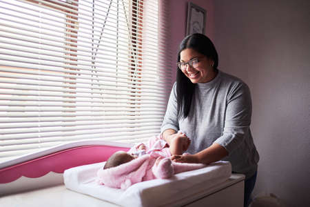Who needs a wardrobe assistant when youve got mom. Shot of a young woman changing her baby girls clothing at home.の写真素材