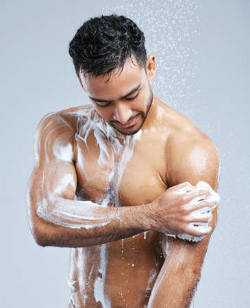 Lather up and scrub. Studio shot of a handsome young man taking a shower against a grey background.の写真素材