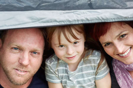 Escaping to the great outdoors as a family. Portrait of a cute little girl and her parents sitting inside a tent together.の写真素材