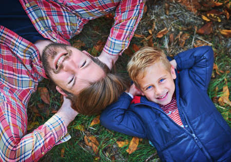 Like father, like son. High angle portrait of a handsome young man and his son lying on the grass outside during autumn.の写真素材