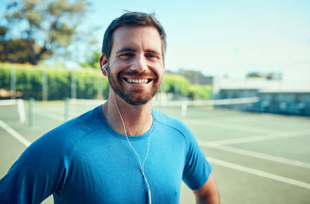 As an athlete, fitness always comes first. Portrait of a sporty young man listening to music while exercising on a tennis court.の写真素材