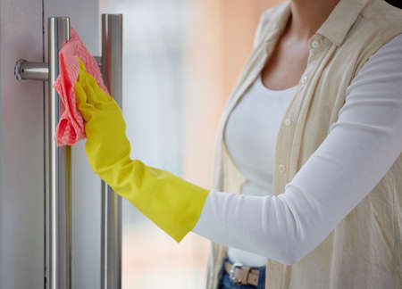 Everything your hands touch should be clean. Shot of a woman cleaning the handles of her door.の写真素材