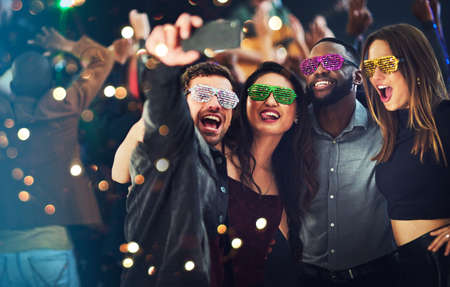 Just because we like to party. Cropped shot of a diverse group of young friends taking a selfie together at a party at night.の写真素材