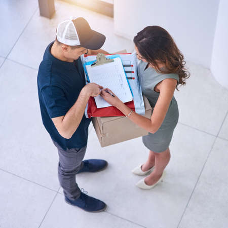 Leave your name and signature over here. Shot of a courier making a delivery to a businesswoman in...