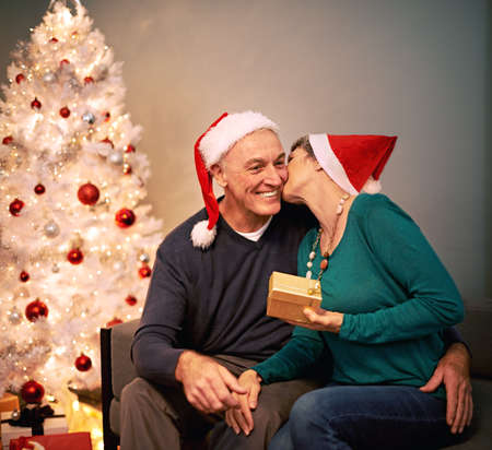 Its definitely more fun to give. A happy mature couple exchanging Christmas gifts in front of their Christmas tree.の写真素材