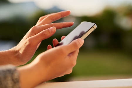 Connected on the go. Closeup shot of an unrecognisable woman using a cellphone outside.の写真素材