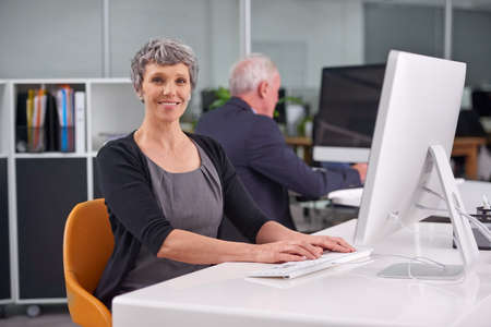 Facing each work day with optimism. Portrait of a smiling mature businesswoman at her desk with a...