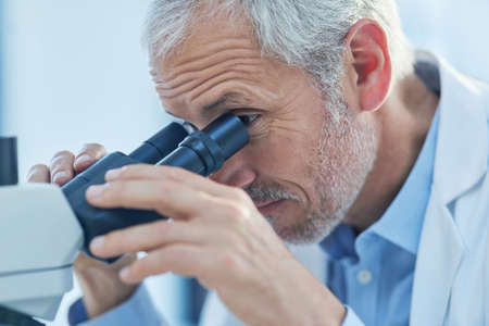 Hes just made a life-changing discovery. Closeup shot of a male scientist looking through a microscope in a lab.の写真素材