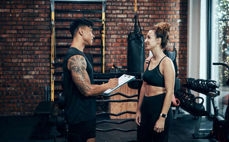 Signup with us, you wont regret it. Shot of a sporty young woman talking to a fitness trainer at the gym.の写真素材