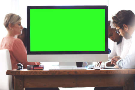 Here to get creative. Shot of a computer with a green screen on a table in an office with businesspeople in the background.の写真素材