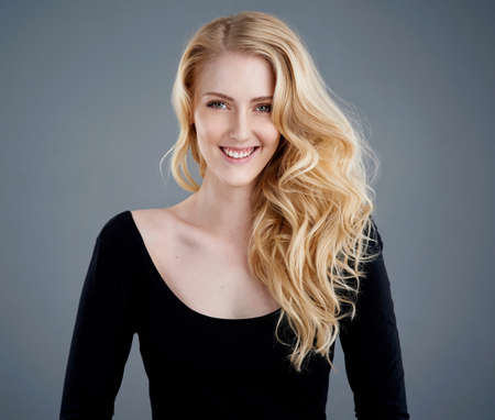 Hair as luminous as the sun. Studio portrait of an attractive young woman with beautiful long blonde hair posing against a gray background.の写真素材